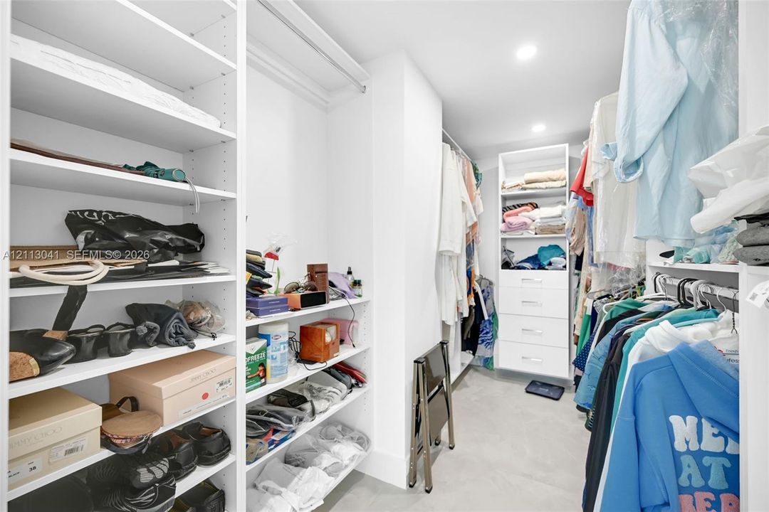 Custom walk-in closet featuring extensive white built-in shelving, multiple hanging rods, and integrated storage drawers with minimalist hardware