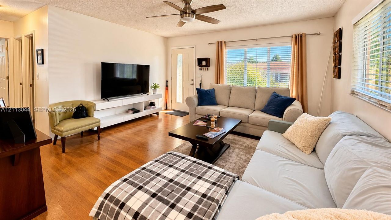 Living area featuring wood-finish flooring, a ceiling fan, and large windows with horizontal blinds