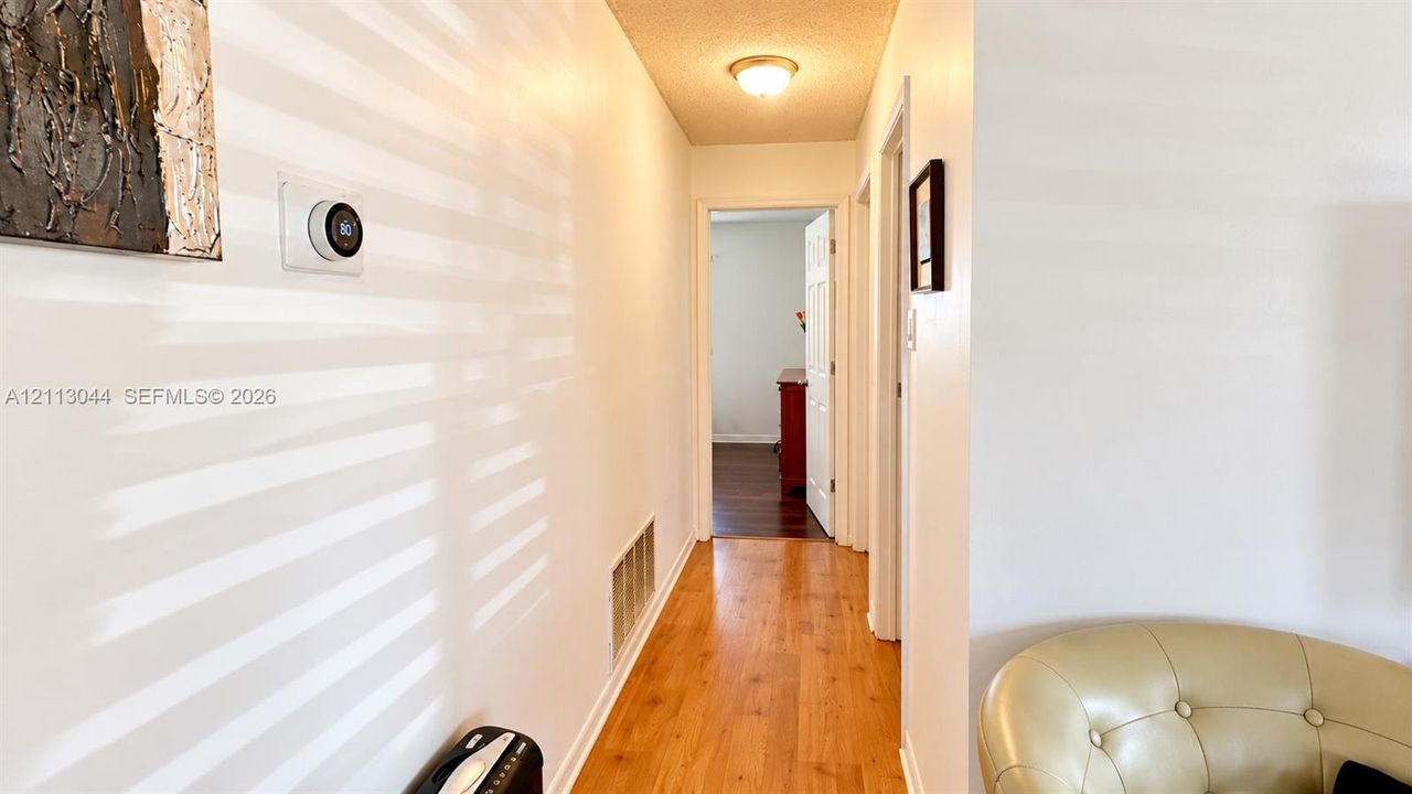 Hallway featuring wood-finish flooring, white walls, flush-mount ceiling lighting, and a smart thermostat