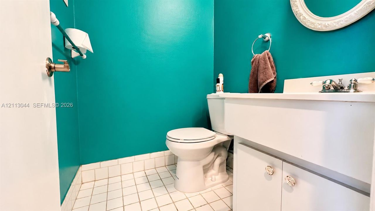 Bathroom featuring white cabinetry, an integrated sink with polished chrome hardware, a wall-mounted oval mirror, and tiled flooring
