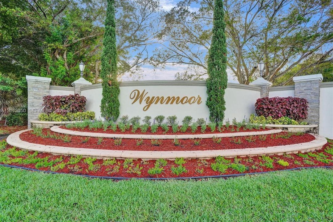 Community entrance monument featuring a curved stucco wall with stone-veneered pillars, tiered landscaping, and manicured ornamental plantings