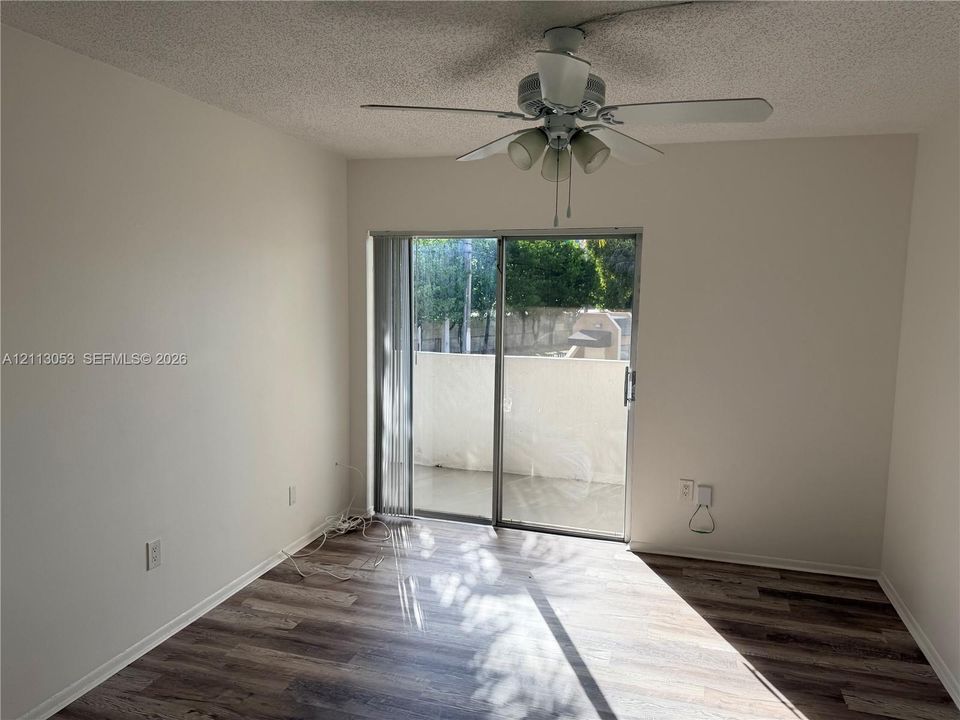 Room featuring wood-finish flooring, a ceiling fan with integrated lighting, and a sliding glass door with vertical blinds