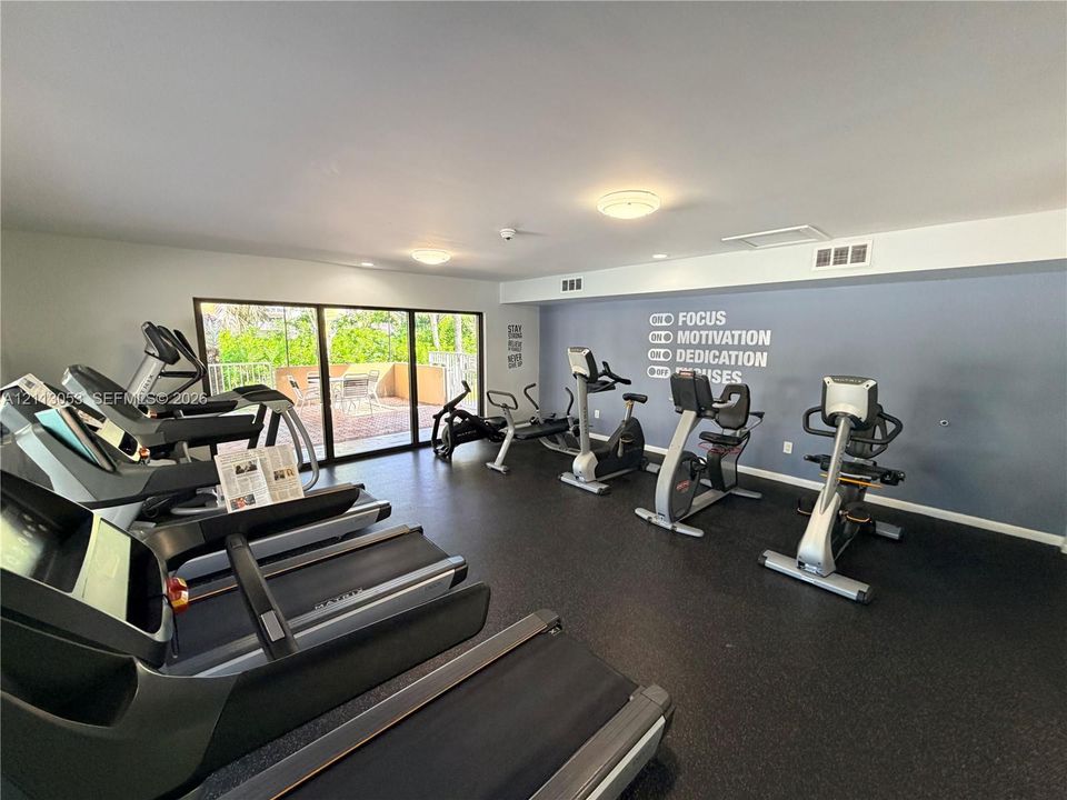 Fitness room with resilient rubber flooring, flush-mount ceiling lighting, and expansive sliding glass doors