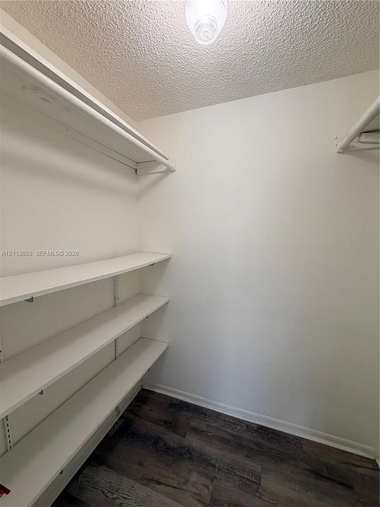 Storage space featuring wood-finish flooring, white walls, adjustable shelving, and a ceiling-mounted light fixture