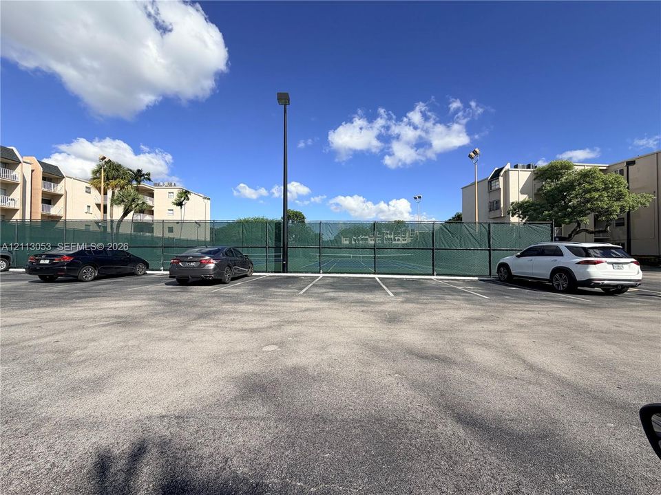 Paved parking area featuring a chain-link fenced recreation court with overhead lighting