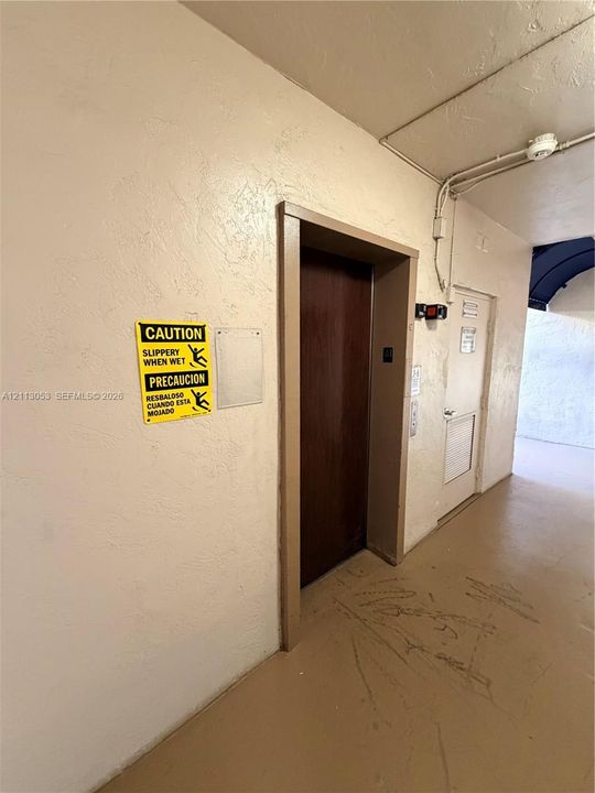 Elevator access with a dark wood-finish door, textured wall surfaces, and a secondary entry door with a louvered panel