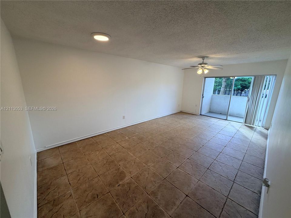 Interior space featuring large-format textured tile flooring, ceiling fan with integrated lighting, recessed lighting, and sliding glass doors with access to an exterior balcony