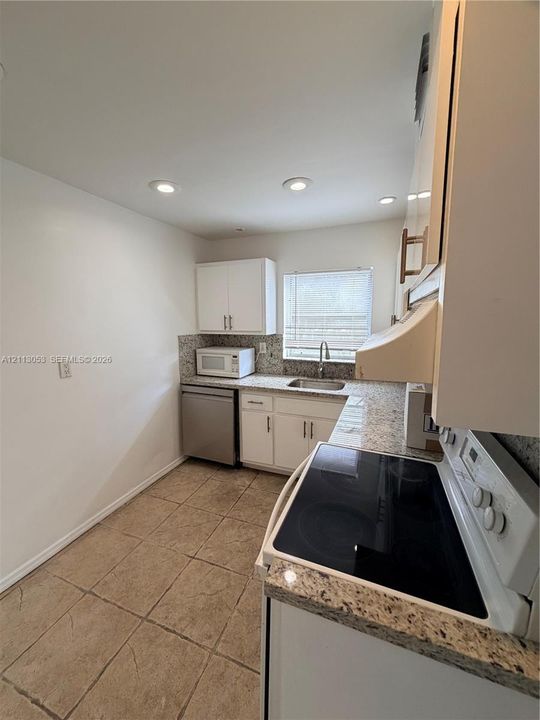 Kitchen featuring white cabinetry, stone-finish countertops, stainless steel appliances, a recessed sink, and tile flooring