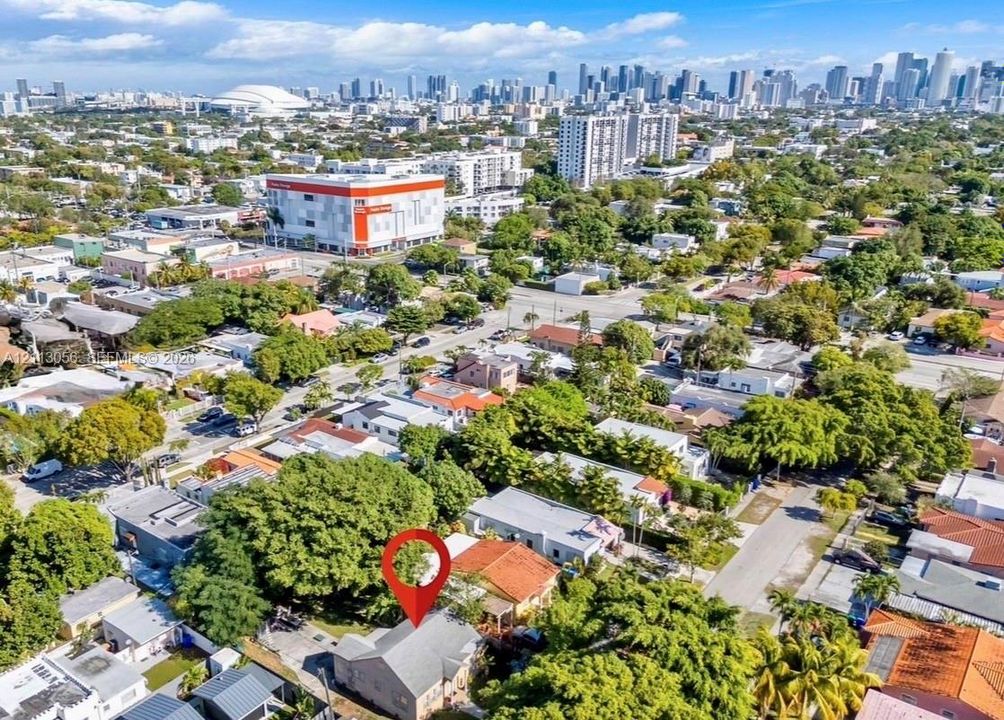 Aerial perspective of a detached residential property featuring a pitched roof, mature canopy trees, and proximity to an urban skyline