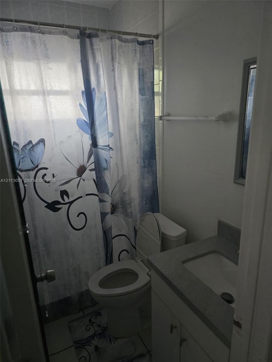 Bathroom featuring a vanity with a solid-surface countertop, an integrated sink, a ceramic tile tub surround, and a wall-mounted towel bar