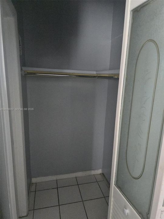 Closet featuring tiled flooring, a built-in shelving unit with a metal garment rod, and a door with an etched glass panel insert