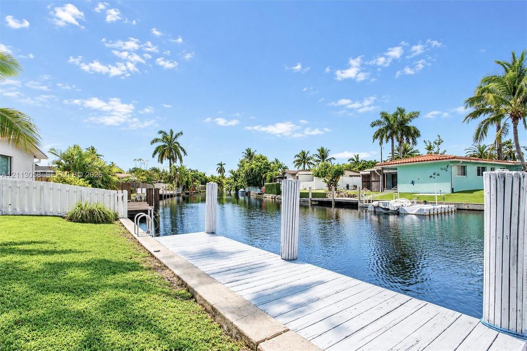 Waterfront property featuring a private white-painted wooden dock, bulkhead sea wall, manicured lawn, and perimeter fencing