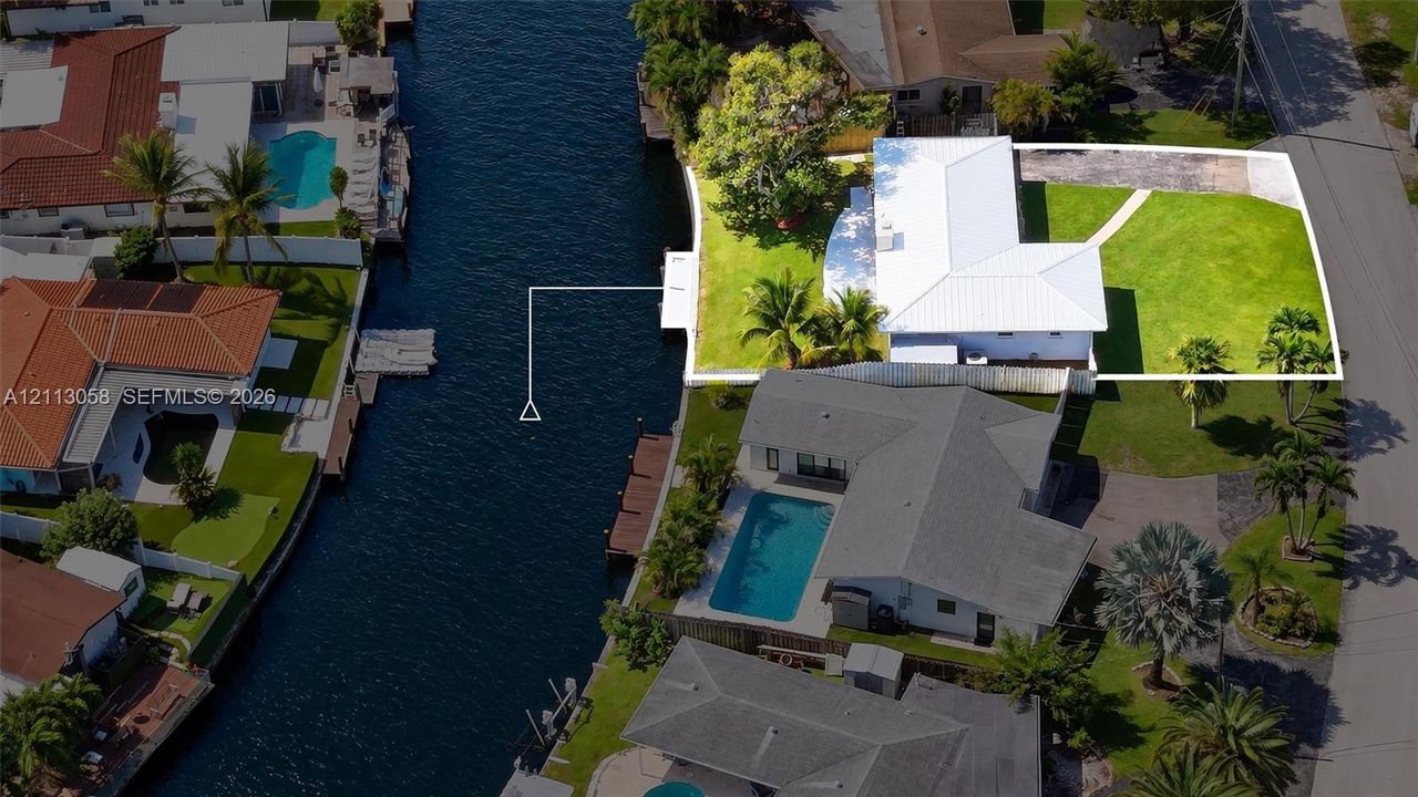 Waterfront property featuring a private dock, expansive lawn, paved driveway, and mature landscaping