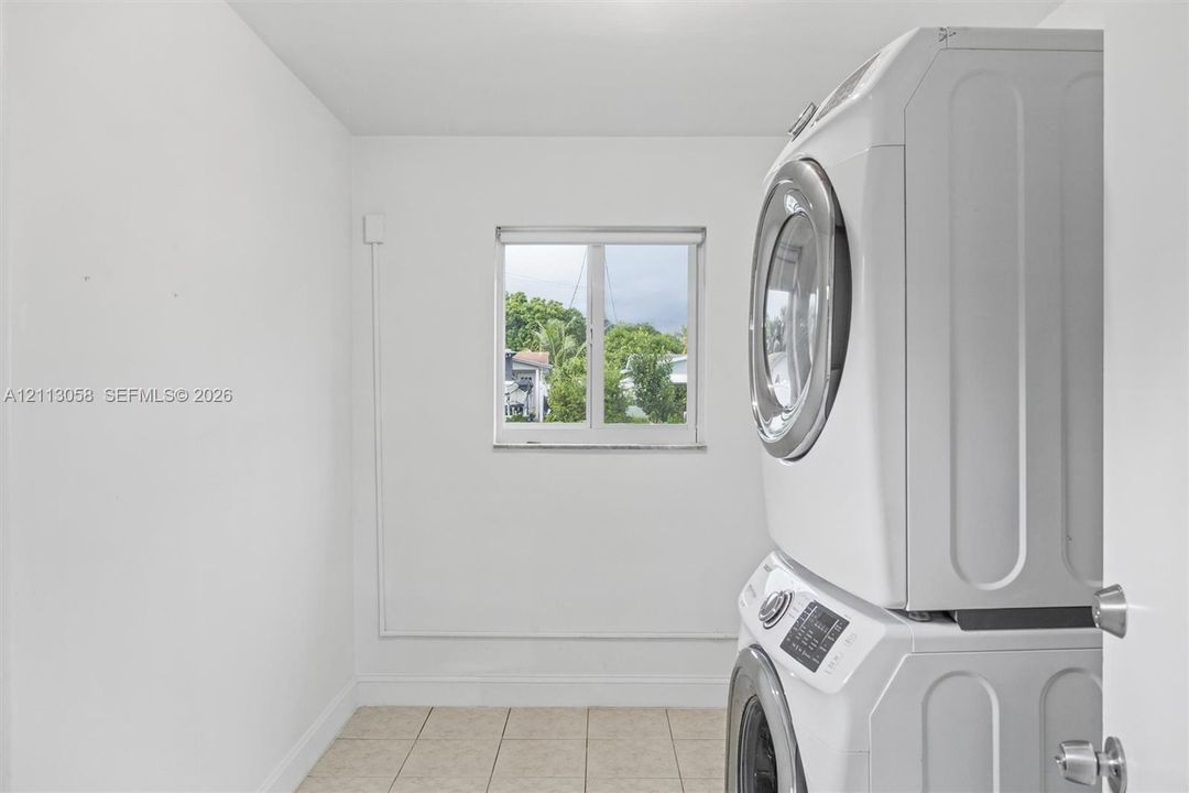 Utility area featuring a stacked washer and dryer unit, neutral ceramic tile flooring, and a window providing natural light