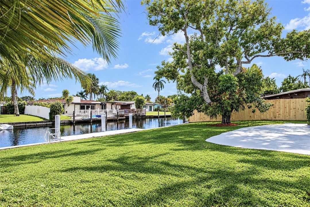 Waterfront backyard featuring a concrete dock, private canal bulkhead, mature trees, and a paved patio area