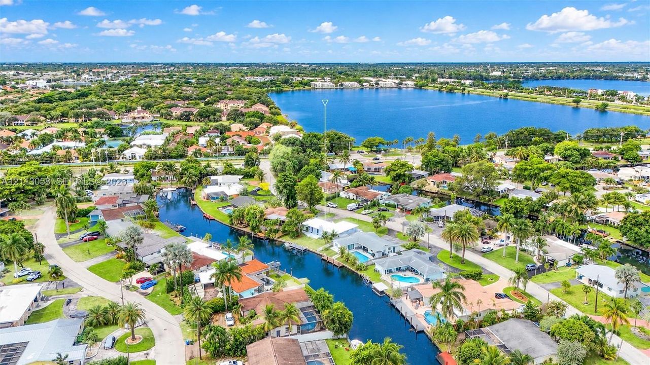 Aerial view of waterfront property featuring canal access, private swimming pool, light-colored roof, and proximity to expansive lake