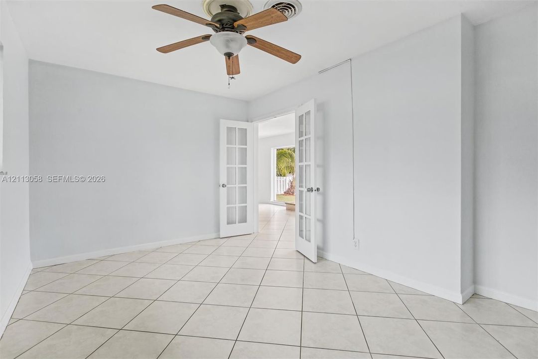 Interior space featuring large-format diagonal tile flooring, white French doors with glass panes, and a ceiling-mounted fan with wood-finish blades