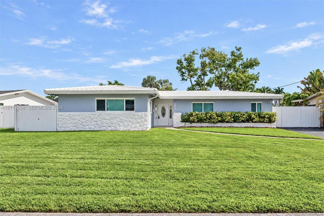 Single-story exterior featuring light-toned masonry, textured stone wainscoting, a covered entry with an oval-glass door, and vinyl perimeter fencing