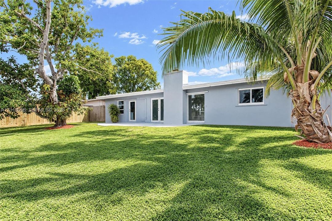 Expansive rear yard featuring a manicured lawn, concrete patio, exterior chimney, and mature trees