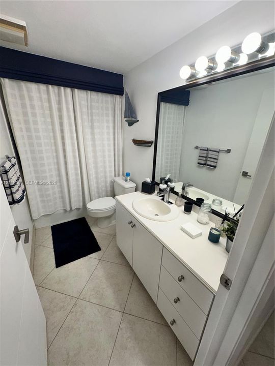 Bathroom featuring a vanity with a white countertop and oval undermount sink, large wall-mounted mirror, multi-bulb light fixture, and stone-finish floor tile