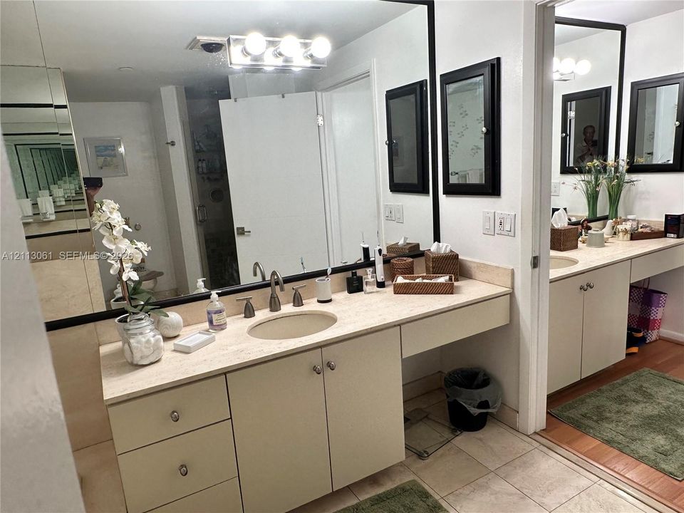 Bathroom featuring a dual-vanity setup with stone countertops, undermount sinks, wall-to-wall mirrors, and built-in cabinetry with metallic hardware