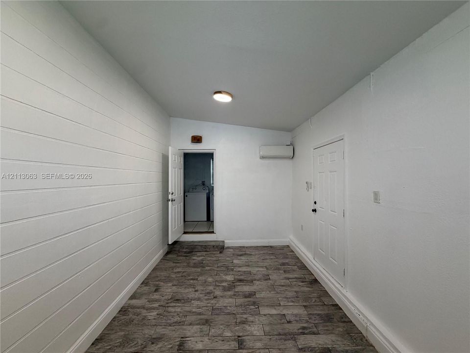 Interior space featuring horizontal plank wall detailing, tile flooring, two paneled doors, and a wall-mounted climate control unit