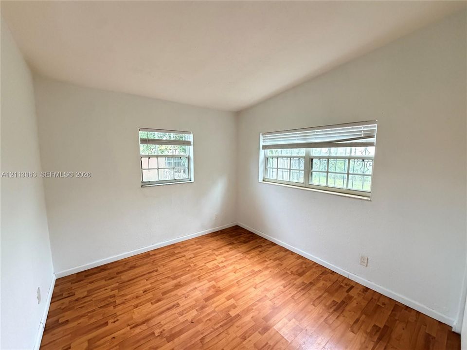 Vaulted ceiling room featuring wood-finish flooring, white walls, and multiple multi-pane windows