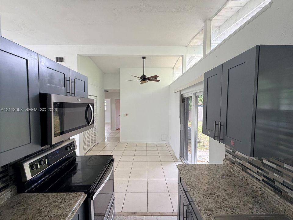 Kitchen featuring shaker-style cabinetry, stone-finish countertops, tile flooring, stainless steel microwave, and clerestory windows