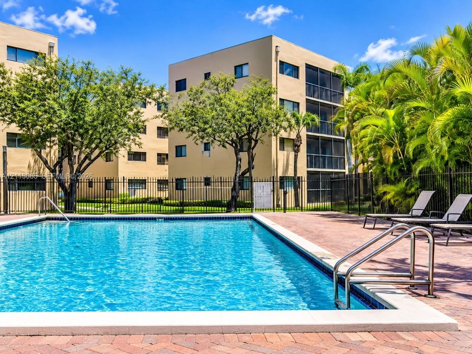 In-ground swimming pool featuring a brick-paver deck, metal pool ladder, and perimeter fencing