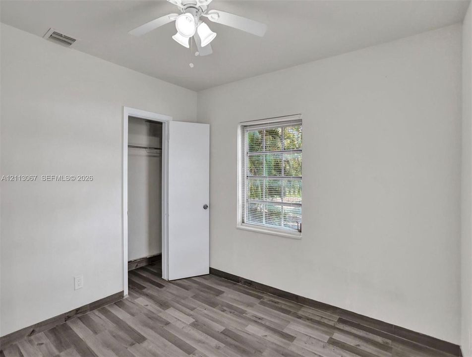 Neutral-toned wall finish, wood-finish flooring, multi-pane window, and a ceiling-mounted light fixture with a fan