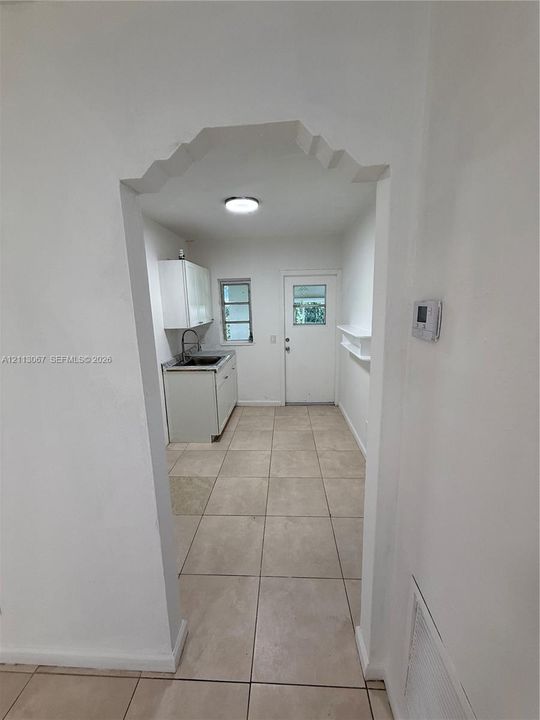 Arched entryway leading to a space featuring neutral-toned tile flooring, built-in lower cabinetry, a mounted sink with a gooseneck faucet, and an exterior door with a window insert