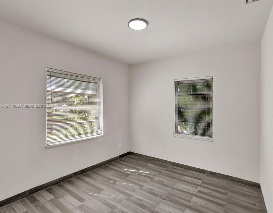 Interior space featuring wood-finish flooring, two windows with horizontal blinds, and a flush-mount ceiling light fixture