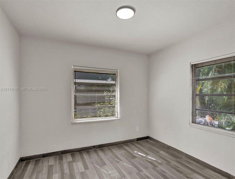 Room featuring wood-finish flooring, neutral walls, two windows with horizontal blinds, and a flush-mount ceiling light fixture