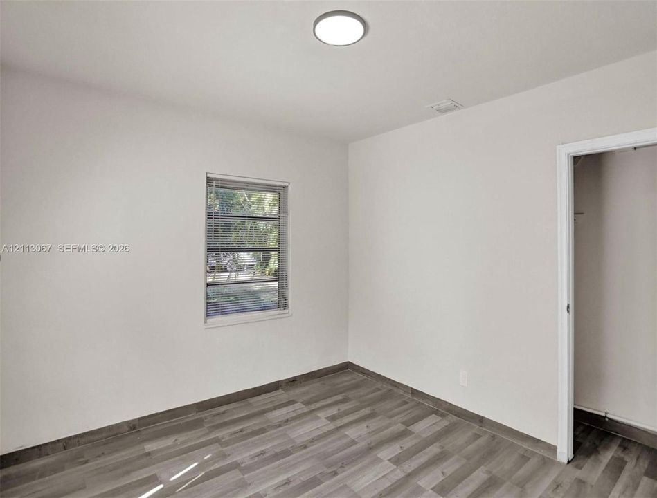 Neutral-toned room featuring wood-finish flooring, a single-pane horizontal sliding window, a circular flush-mount ceiling light, and an interior reach-in closet