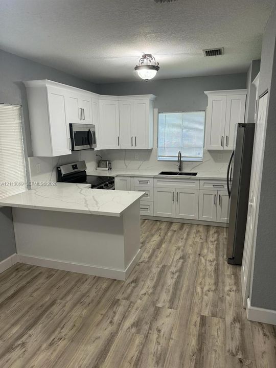 Kitchen featuring white cabinetry, stone-look countertops with integrated backsplash, wood-finish flooring, stainless steel appliances, and a peninsula counter