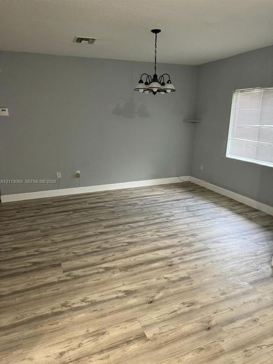 Room featuring wood-finish flooring, a multi-arm chandelier, and a window with integrated blinds