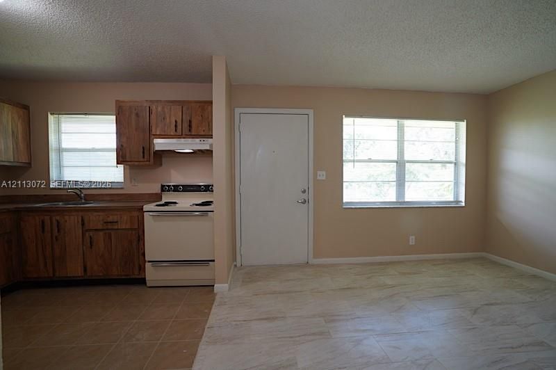 Kitchen featuring wood cabinetry, integrated range hood, white freestanding oven, and tile flooring