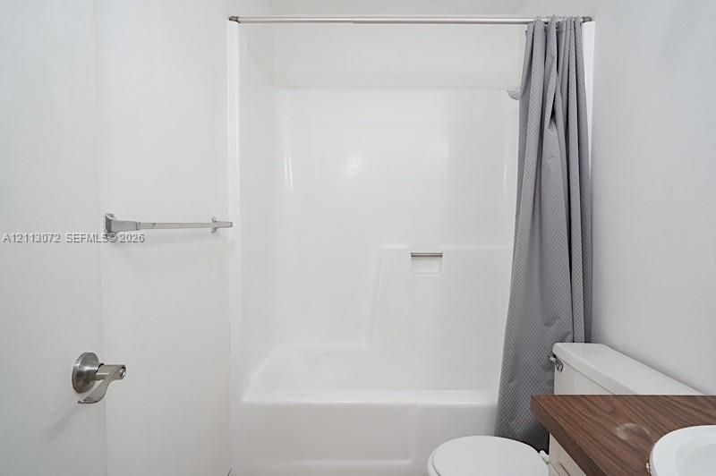 White acrylic tub and shower surround, vanity with a dark wood-finish countertop, and stainless steel hardware