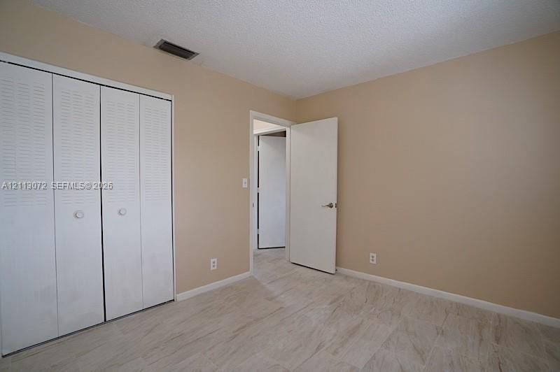 Neutral-toned interior featuring textured ceiling finish, stone-finish tile flooring, and white louvered-panel closet doors