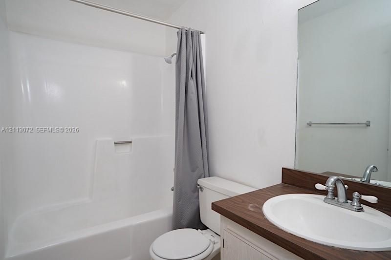 Bathroom featuring a molded composite tub and shower surround, vanity with a wood-finish countertop, integrated oval sink basin, chrome-finished dual-handle faucet, and a wall-mounted mirror