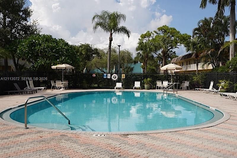 In-ground swimming pool with a curved edge, integrated steps, metal handrails, and a surrounding paver deck enclosed by metal fencing