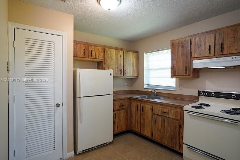 Kitchen featuring wood cabinetry, integrated range hood, tile flooring, and a louvered pantry door