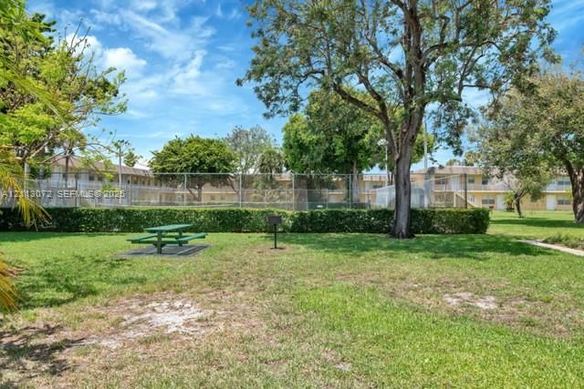 Expansive common green space featuring mature trees, manicured hedges, and a chain-link fenced recreation area