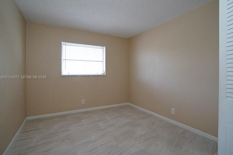 Interior room featuring neutral wall paint, wood-finish tile flooring, a horizontal slider window with blinds, and a louvered closet door