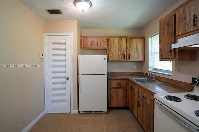 Kitchen featuring wood cabinetry, laminate countertops, stainless steel sink with a metallic faucet, white appliances, and tiled flooring