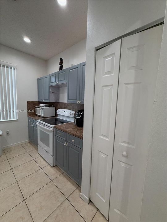 Kitchen featuring gray cabinetry, stone-finish countertops, tile flooring, recessed lighting, and a white bi-fold closet door
