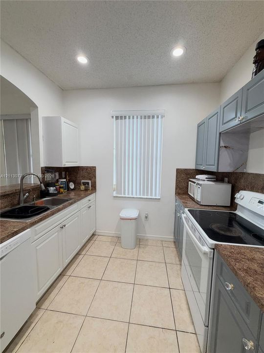 Kitchen featuring contrasting white and slate-toned cabinetry, laminate countertops, recessed lighting, and tile flooring