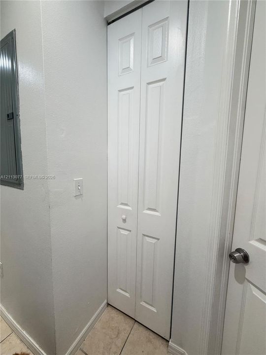 White bifold closet door with six-panel detailing, standard wall-mounted light switch, and light-toned tile flooring