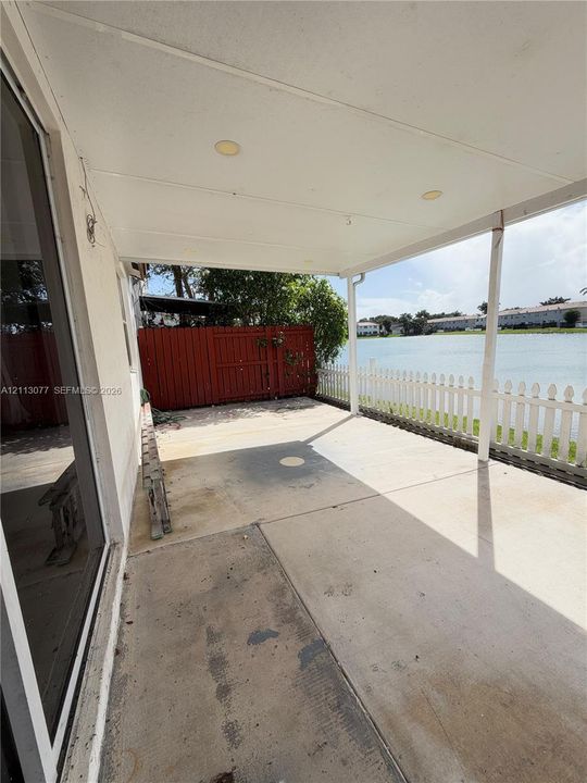 Covered concrete patio featuring recessed lighting, a white picket fence, and red privacy fencing