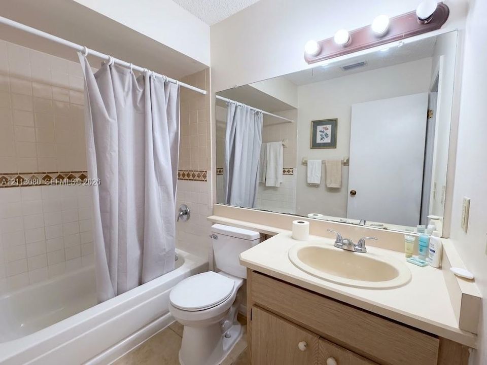 Full-width wall mirror, vanity cabinet with integrated sink, porcelain-finish bathtub with tiled surround, and decorative accent tile border